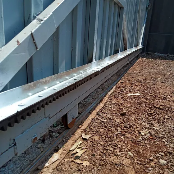 Detalhe da cremalheira parafusada na base do portão deslizante, com o trilho e a roldana no piso