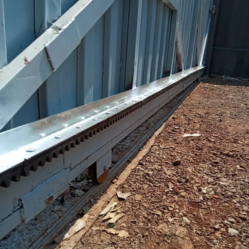 Detalhe da cremalheira parafusada na base do portão deslizante, com o trilho e a roldana no piso