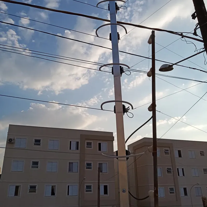 Haste alta de cerca elétrica com isoladores e blocos de apartamentos ao fundo, no fim da tarde