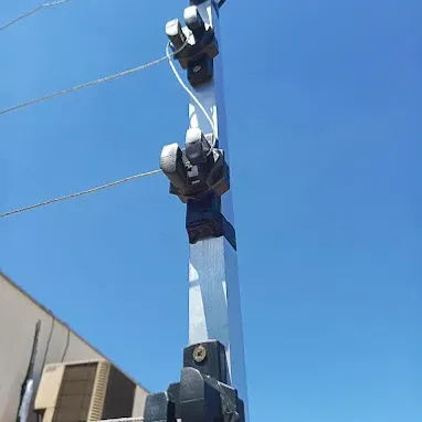 Detalhe de haste galvanizada de cerca elétrica com isoladores e fios, contra o céu azul