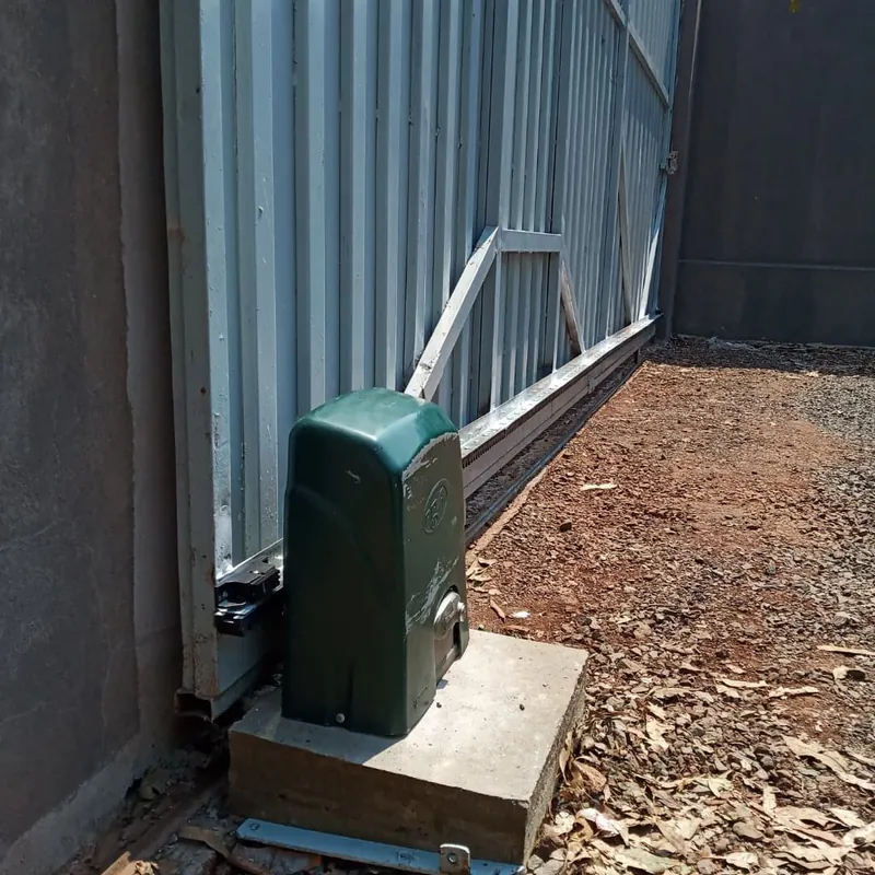 Motor de portão deslizante fixado sobre base de concreto, junto ao trilho e à cremalheira