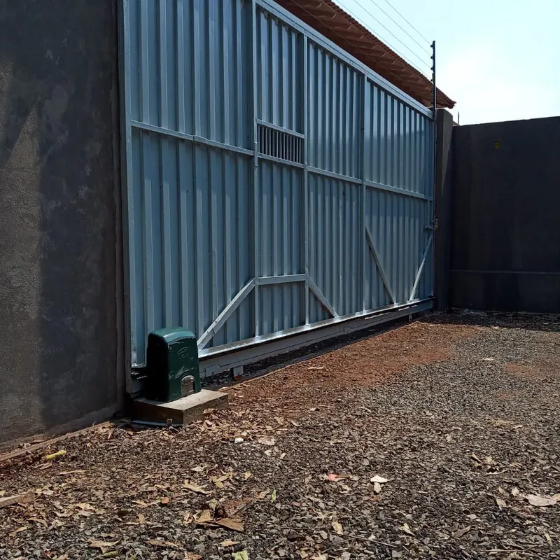 Portão deslizante metálico de galpão com motor instalado na base e muro com cerca elétrica ao fundo